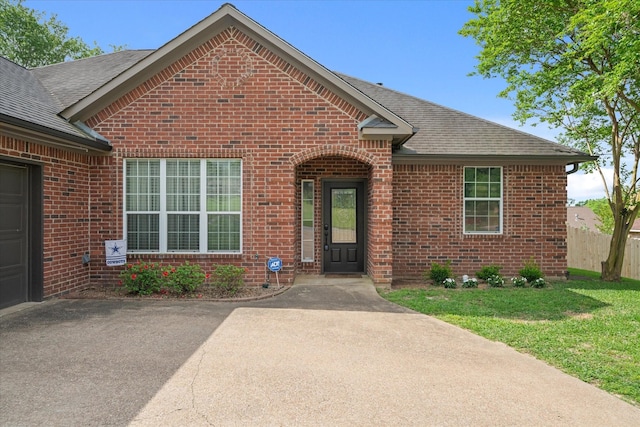 view of front of property with fence, a shingled roof, brick siding, and a front yard