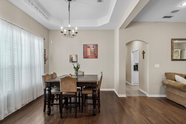 dining space with wood finished floors, arched walkways, a tray ceiling, a notable chandelier, and visible vents