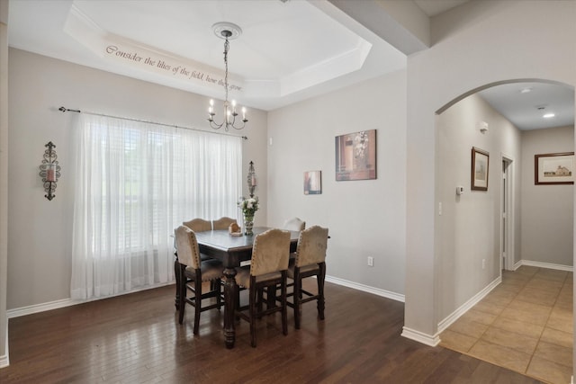 dining room featuring a tray ceiling, wood finished floors, arched walkways, baseboards, and a chandelier