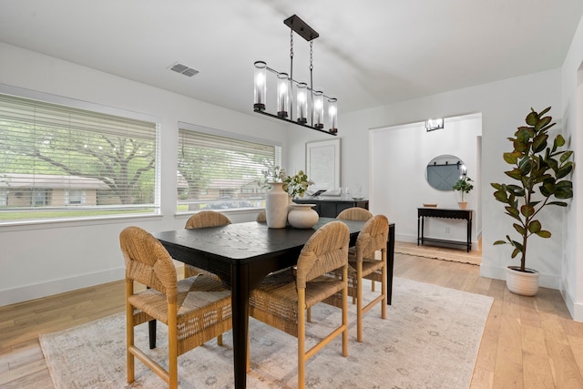 dining room with light wood finished floors, baseboards, visible vents, and an inviting chandelier