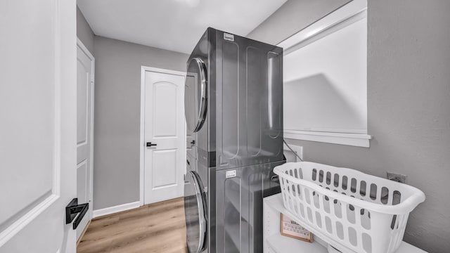 washroom featuring laundry area, baseboards, stacked washer / drying machine, and wood finished floors