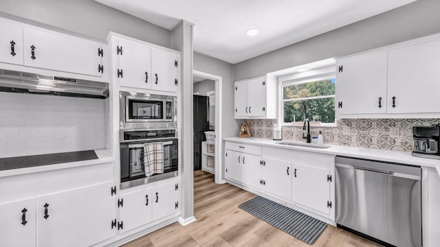 kitchen with a sink, light countertops, stainless steel appliances, decorative backsplash, and under cabinet range hood