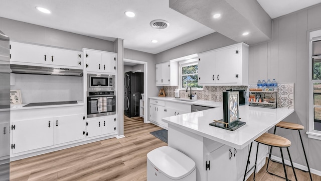 kitchen with decorative backsplash, light countertops, under cabinet range hood, a sink, and appliances with stainless steel finishes