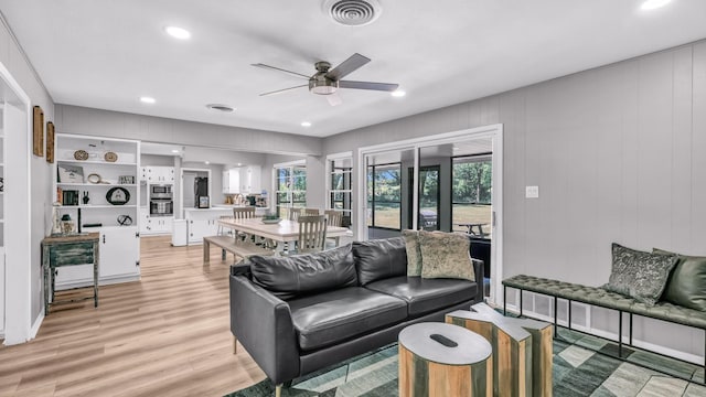 living area with a wealth of natural light, a ceiling fan, light wood finished floors, and visible vents