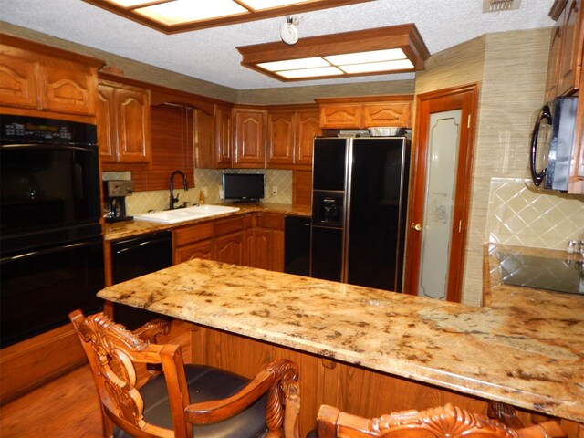kitchen featuring a kitchen breakfast bar, a sink, decorative backsplash, black appliances, and brown cabinetry