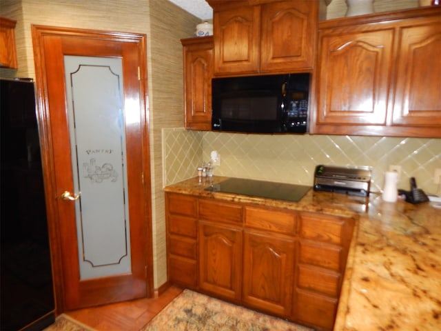 kitchen featuring backsplash, brown cabinets, light stone counters, and black appliances
