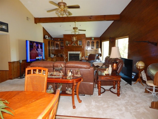 carpeted living area with a wainscoted wall, vaulted ceiling with beams, wood walls, ceiling fan, and a fireplace