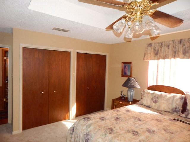 bedroom with two closets, visible vents, carpet flooring, and ceiling fan