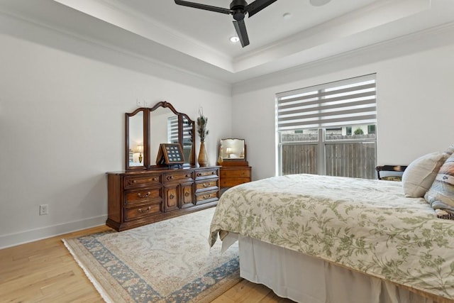 bedroom with recessed lighting, a tray ceiling, wood finished floors, crown molding, and baseboards