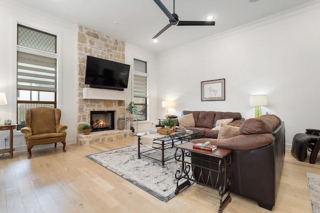 living room with light wood-style flooring, baseboards, ceiling fan, a stone fireplace, and ornamental molding