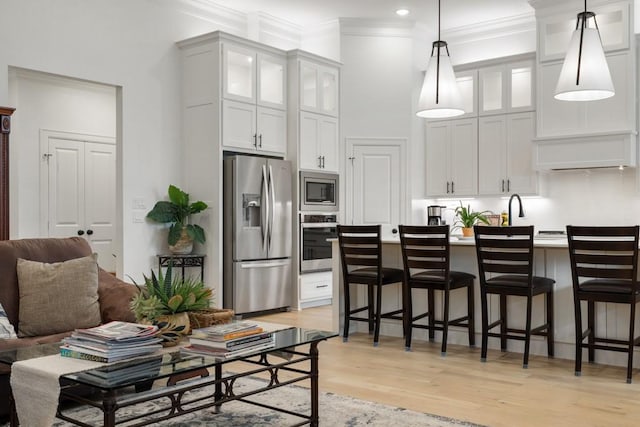 kitchen with glass insert cabinets, appliances with stainless steel finishes, a breakfast bar, and light wood-type flooring