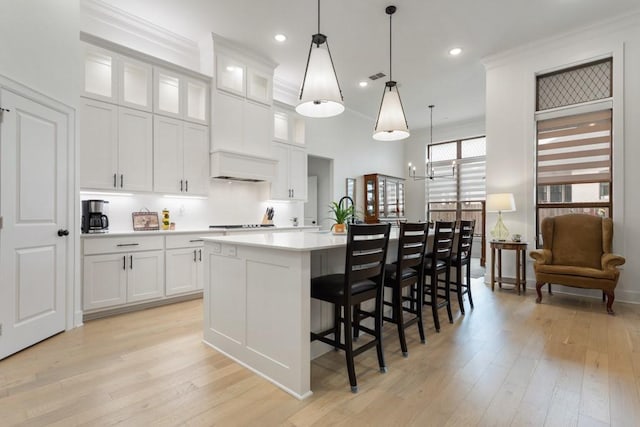 kitchen with light countertops, light wood-style flooring, a center island with sink, and white cabinetry