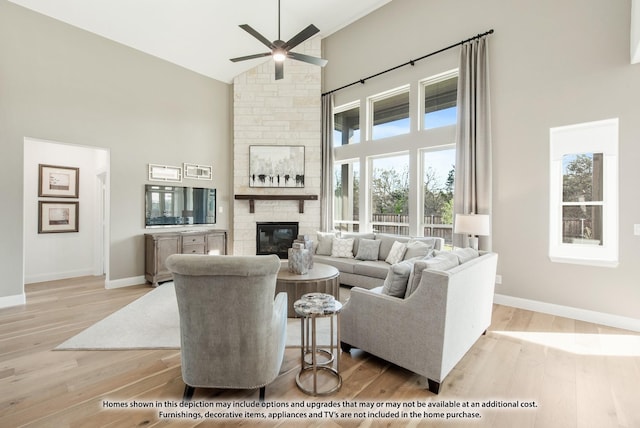 living room with high vaulted ceiling, a ceiling fan, wood finished floors, a stone fireplace, and baseboards