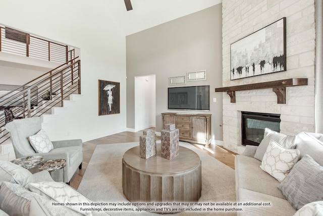 living area with high vaulted ceiling, a stone fireplace, wood finished floors, stairs, and baseboards