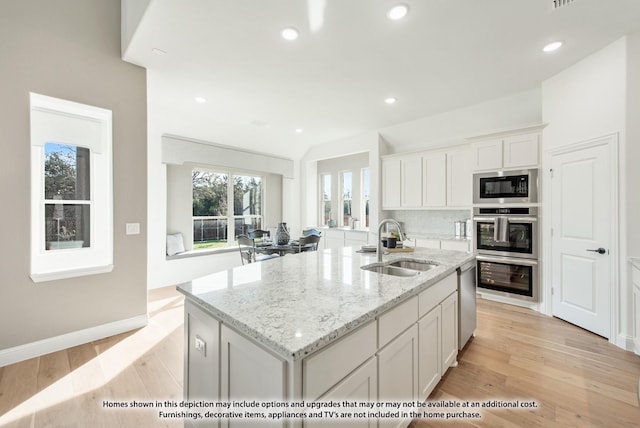 kitchen featuring light stone counters, a sink, light wood-style floors, a center island with sink, and white cabinetry