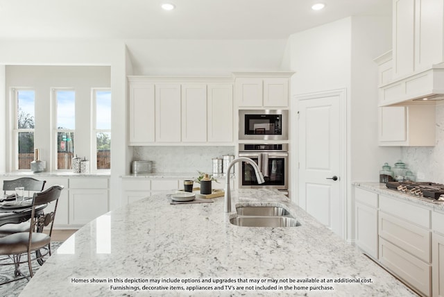 kitchen with white cabinets, appliances with stainless steel finishes, light stone countertops, and a sink