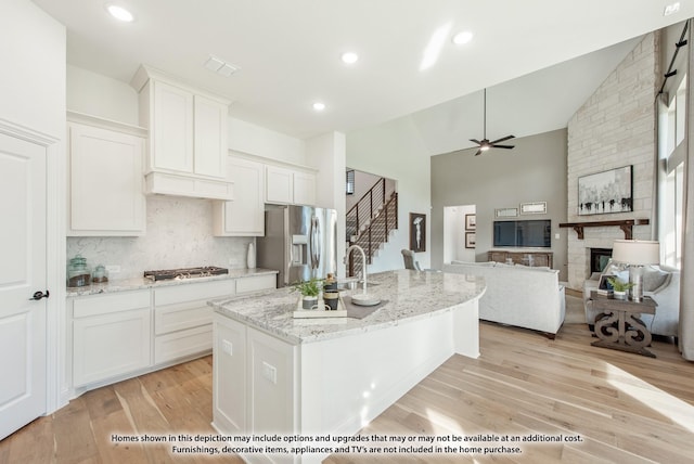kitchen with ceiling fan, a stone fireplace, white cabinetry, and stainless steel appliances