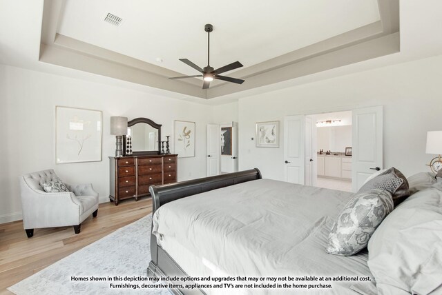 bedroom with ensuite bath, light wood-style flooring, visible vents, and a raised ceiling