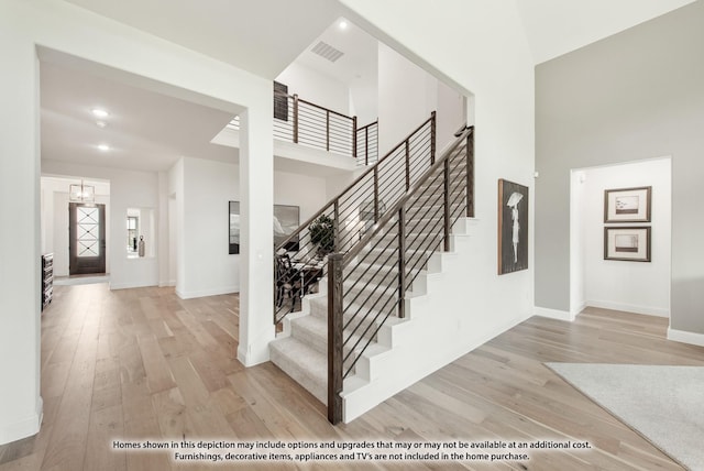 staircase with a high ceiling, wood finished floors, visible vents, and baseboards