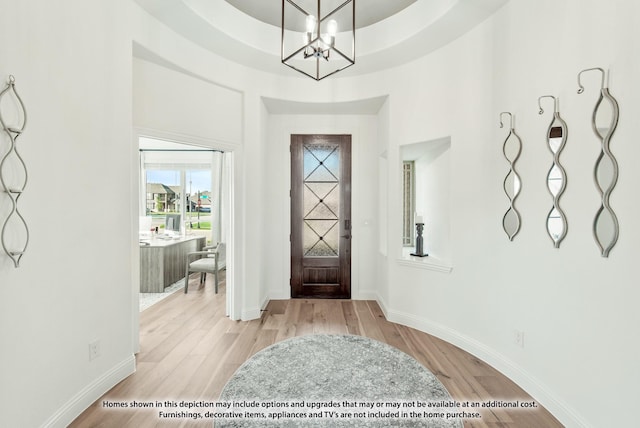 entryway with light wood-style floors, a towering ceiling, baseboards, and an inviting chandelier