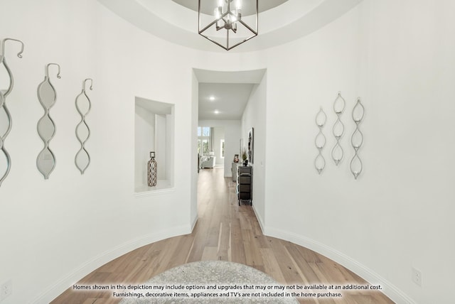 corridor with light wood-style flooring, baseboards, and a notable chandelier