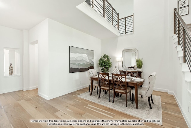 dining room with stairway, baseboards, a high ceiling, and light wood-style flooring