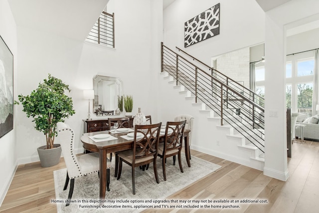 dining space with baseboards, light wood-type flooring, a high ceiling, and stairs