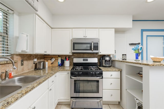 kitchen with stainless steel appliances, a sink, white cabinetry, decorative backsplash, and light tile patterned floors