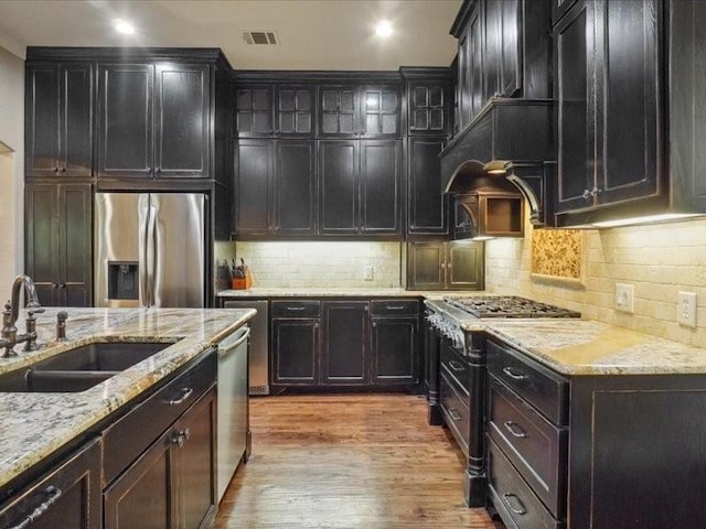 kitchen featuring a sink, tasteful backsplash, wood finished floors, light stone countertops, and appliances with stainless steel finishes