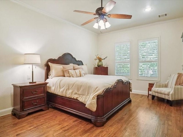 bedroom with baseboards, crown molding, wood finished floors, and visible vents