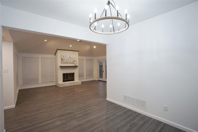 unfurnished living room with dark wood finished floors, baseboards, visible vents, a chandelier, and a fireplace