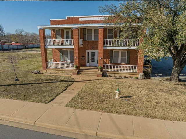 view of front of property with a porch, a front lawn, a balcony, and brick siding