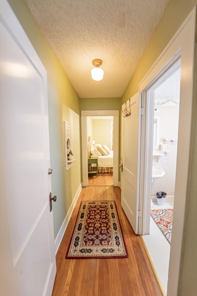 hall featuring light wood-style flooring, baseboards, and a textured ceiling