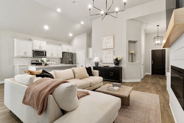 living room with recessed lighting, an inviting chandelier, light wood-style floors, baseboards, and high vaulted ceiling
