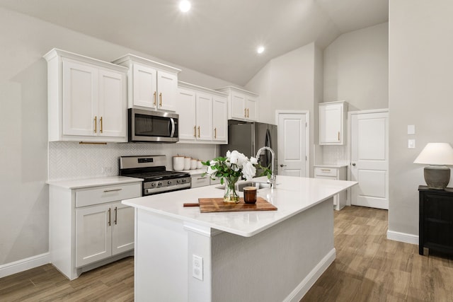 kitchen featuring appliances with stainless steel finishes, backsplash, a sink, white cabinetry, and light wood-type flooring