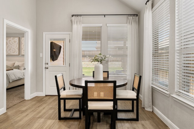 dining area featuring light wood finished floors, lofted ceiling, and baseboards