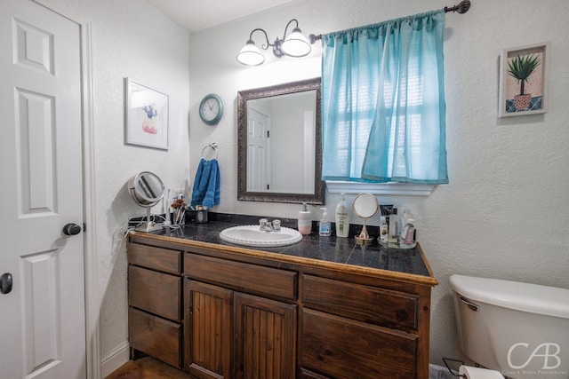 bathroom featuring toilet, a textured wall, and vanity