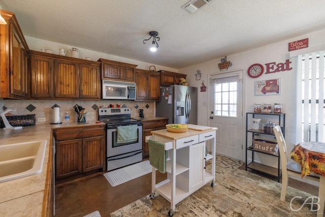 kitchen with stainless steel appliances, a sink, a textured ceiling, tasteful backsplash, and visible vents