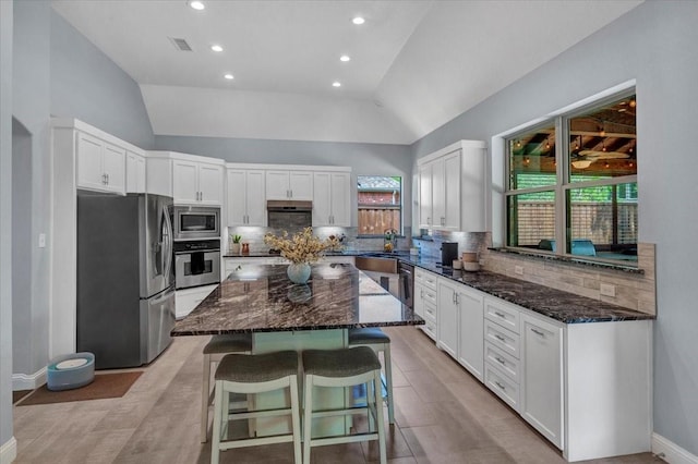 kitchen with lofted ceiling, stainless steel appliances, decorative backsplash, and dark stone counters