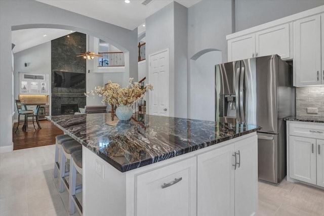 kitchen featuring high vaulted ceiling, ceiling fan, dark stone countertops, and stainless steel fridge