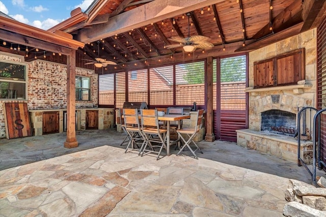 view of patio with exterior kitchen, an outdoor stone fireplace, outdoor dining area, and ceiling fan