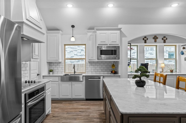 kitchen featuring a center island, a sink, arched walkways, stainless steel appliances, and white cabinets