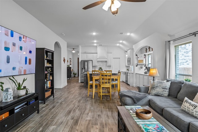 living area with arched walkways, visible vents, lofted ceiling, a ceiling fan, and wood finished floors