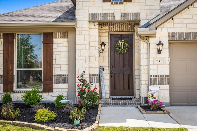 entrance to property with stone siding, roof with shingles, and a garage