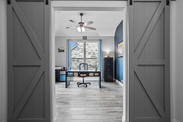 office space featuring a barn door, baseboards, a ceiling fan, and light wood-style flooring