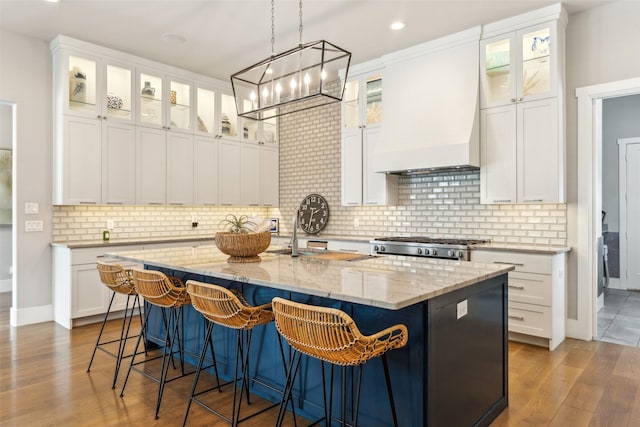 kitchen with custom exhaust hood, an island with sink, a breakfast bar area, white cabinets, and stove