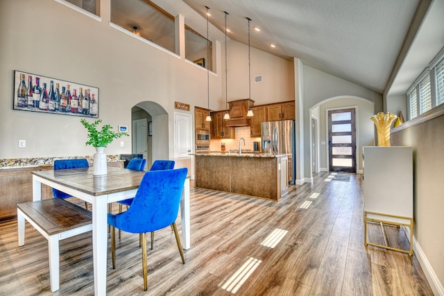 1023 Clydeview Rd, Forney, TX 75126 - dining area featuring light wood finished floors, arched walkways, a textured ceiling, baseboards, and high vaulted ceiling