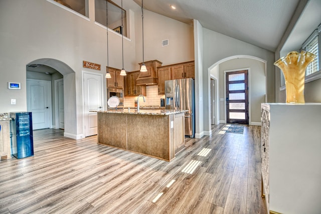 1023 Clydeview Rd, Forney, TX 75126 - kitchen with stainless steel fridge, visible vents, light stone countertops, brown cabinetry, and an island with sink