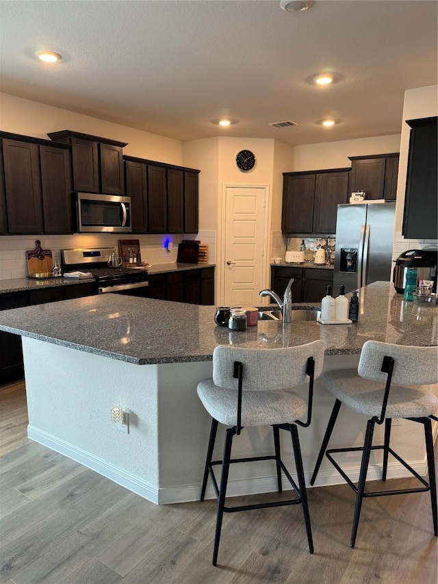 7412 Yearwood Dr, Mckinney, TX 75071 - kitchen featuring a breakfast bar, dark brown cabinets, light wood-type flooring, dark stone counters, and appliances with stainless steel finishes