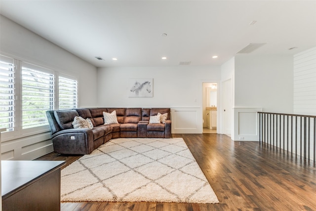 living area with a decorative wall, dark wood-type flooring, visible vents, and recessed lighting